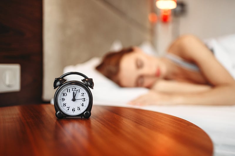 Person using traditional alarm clock instead of phone